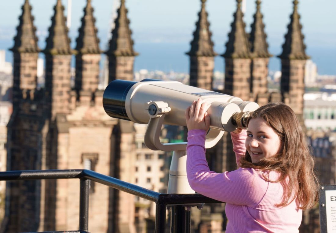 A girl looks through binoculars at Edinburgh skyline from the Rooftop Terrace at Camera Obscura