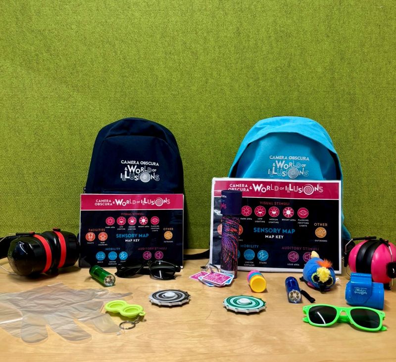 Two backpacks with various support items displayed such as ear defenders, fidget toys, maps and gloves