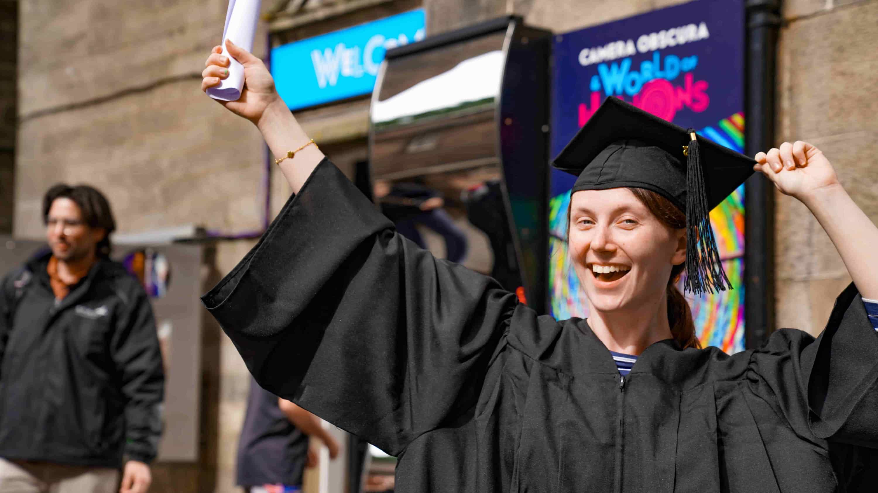 A graduate stands in cap and gown outside Camera Obscura in Edinburgh
