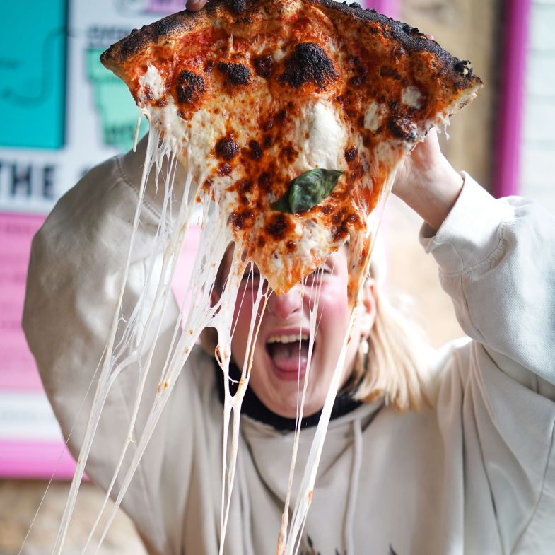 A girl holds up a large slize of pizza with stringy cheese