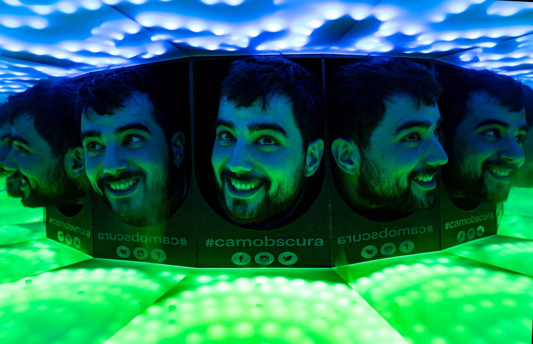 A man has his head in a mirrored box with blue and green lighting at Camera Obscura 