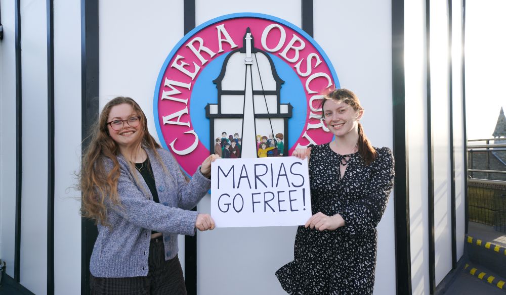 Girls stand on the Rooftop at Camera Obscura, Edinburgh, holding a sign saying 'Maria's Go Free'