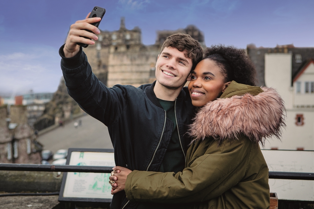 A couple take a selfie with Edinburgh Castle from the Rooftop Terrace at Camera Obscura